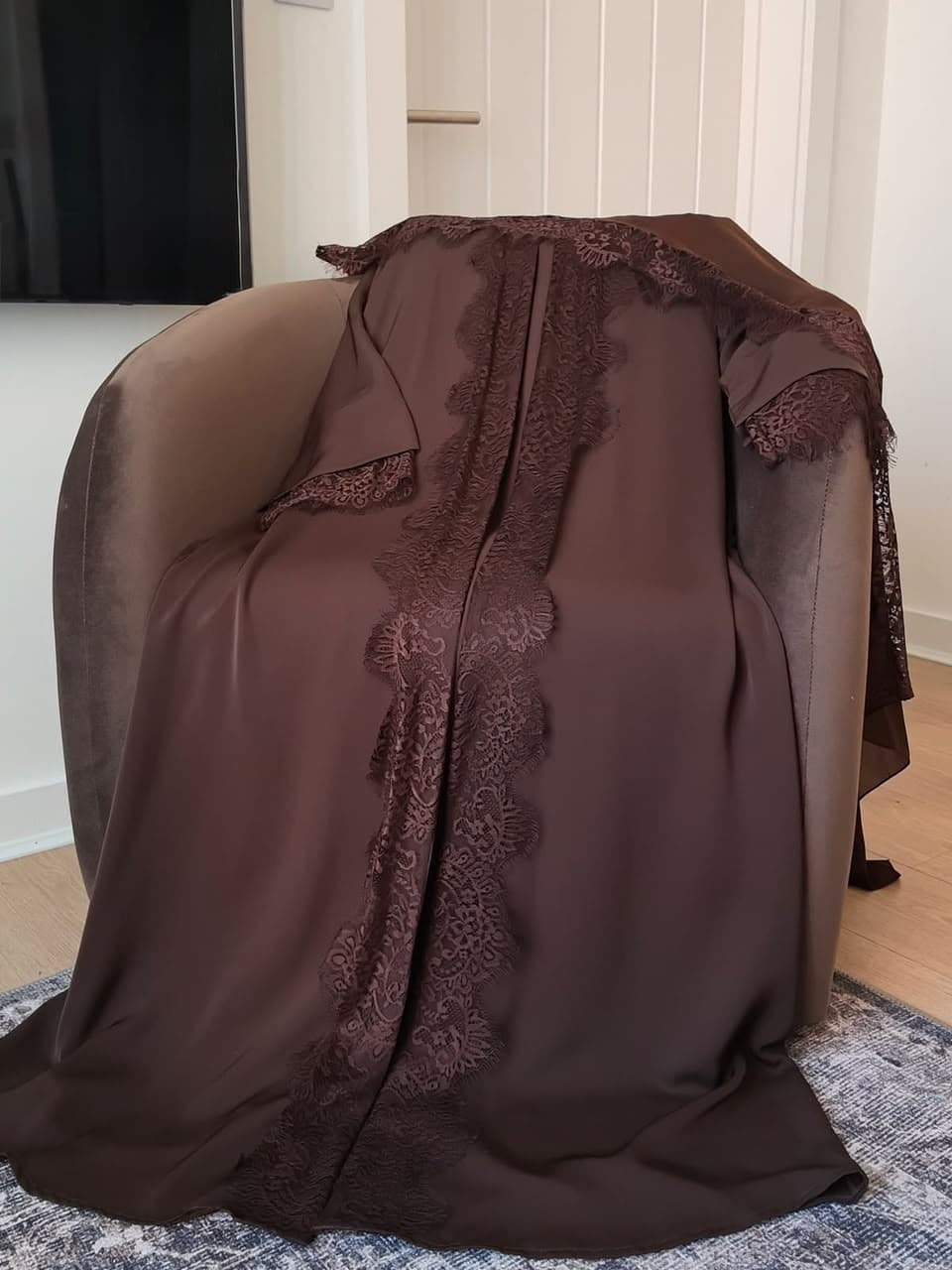 Chocolate brown lace-trimmed abaya draped over a velvet armchair